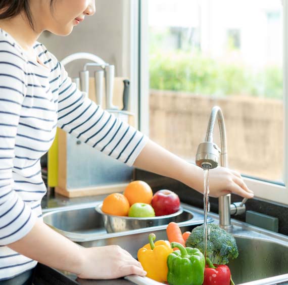 a woman at the sink rinsing vegetables under the faucet